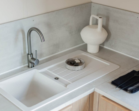 Moderne spoelbak en kraan bij een glampingverblijf, met strak werkblad en keramische decoratie.