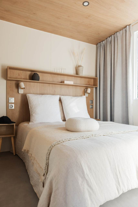 Sfeervolle glampingkamer met tweepersoonsbed, houten plafond en minimalistische en natuurlijke inrichting.