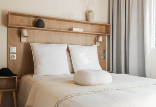 Sfeervolle glampingkamer met tweepersoonsbed, houten plafond en minimalistische en natuurlijke inrichting.