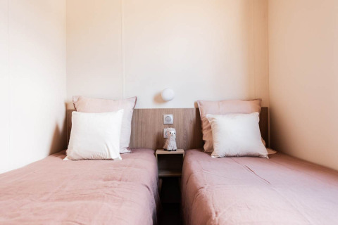 Two single beds with pink bedding and white pillows at Sunset Lodge, cozy décor, soft lighting.