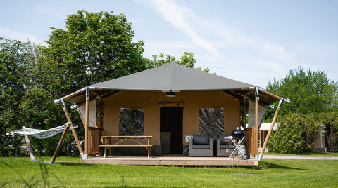 Safari-telt ved navn Cottage med veranda, hængekøje, siddepladser og grill på en grøn græsplæne.