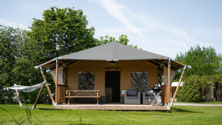 Tente safari nommée Cottage avec véranda, hamac, espace salon et barbecue sur pelouse verte.