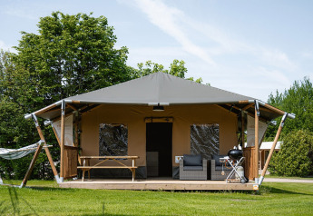 Safari-Zelt namens Cottage mit Veranda, Hängematte, Sitzgelegenheiten und Grill auf grünem Rasen.
