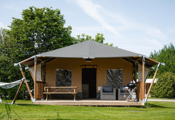 Safari-telt ved navn Cottage med veranda, hængekøje, siddepladser og grill på en grøn græsplæne.
