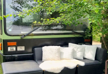 Buitensofa met witte kussens voor de groene mobihome REEBUS onder bomen in België.
