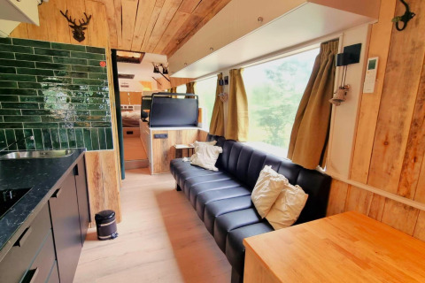 Moderne mobilhomeinteriør i REEBUS, Belgien, med sort sofa, grønne fliser og store vinduer.