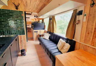 Moderne mobilhomeinteriør i REEBUS, Belgien, med sort sofa, grønne fliser og store vinduer.