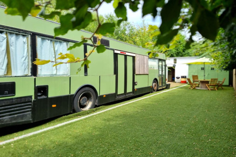 Grønt mobilhome kaldet REEBUS parkeret på en kunstgræsplæne i Belgien med havemøbler i baggrunden.