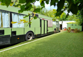 Grønt mobilhome kaldet REEBUS parkeret på en kunstgræsplæne i Belgien med havemøbler i baggrunden.