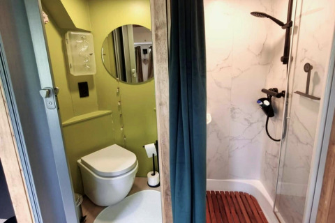 Moderne badkamer in REEBUS mobilhome in België, met douche, toilet, ronde spiegel en gordijn als scheiding.