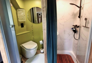 Moderne badkamer in REEBUS mobilhome in België, met douche, toilet, ronde spiegel en gordijn als scheiding.