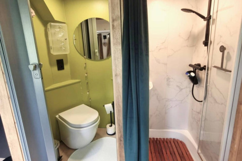 Moderne mobilhome-badeværelse i REEBUS Belgien med brusekabine, toilet og spejl, opdelt med gardin.