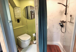 Moderne mobilhome-badeværelse i REEBUS Belgien med brusekabine, toilet og spejl, opdelt med gardin.
