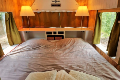 Knusse slaapkamer in het REEBUS-mobiel thuis in België, met tweepersoonsbed en groene gordijnen.