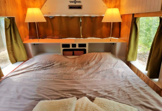 Knusse slaapkamer in het REEBUS-mobiel thuis in België, met tweepersoonsbed en groene gordijnen.