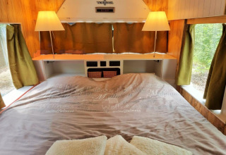 Soveområde i mobilhjemmet REEBUS i Belgien med dobbeltseng, grønne gardiner og hyggelig belysning.