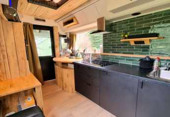 Modern keukeninterieur van een mobilhome met groene tegels en houten accenten in REEBUS, België.