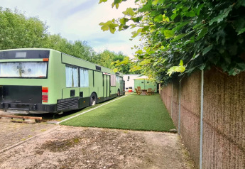 Groene REEBUS mobiele woning, omgebouwd van bus, op kunstgras met tuinmeubels en heg ernaast.