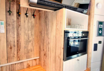 Keukenhoek in de REEBUS-mobiele woning in België met houten panelen, oven, glazen en kleurige haken.
