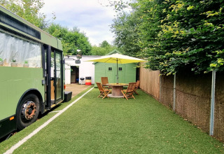 Afbeelding van mobilhome REEBUS in België met groene bus, tuintafel, stoelen en groen tuinhuisje.
