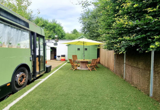 Billede af mobilhjemmet REEBUS i Belgien med grøn bus, havebord, stole og et grønt skur i baggrunden.