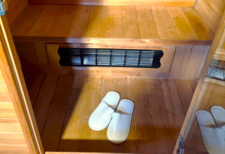Binnen in de REEBUS-mobilhome in België met houten vloer, bank, ventilatierooster en witte pantoffels.
