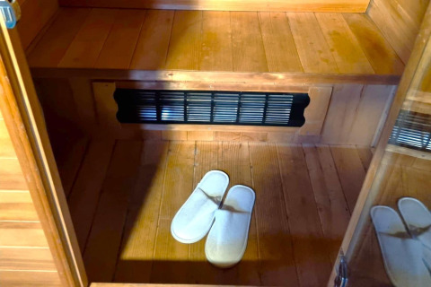 Inde i REEBUS mobilhome i Belgien med trægulv, bænk, ventilationsrist og hvide hjemmesko på gulvet.