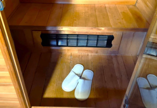 Inde i REEBUS mobilhome i Belgien med trægulv, bænk, ventilationsrist og hvide hjemmesko på gulvet.