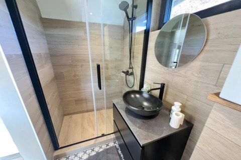 Baño moderno en Pine Tree Tiny Cottage en Bélgica, con ducha, lavabo negro y espejo redondo.