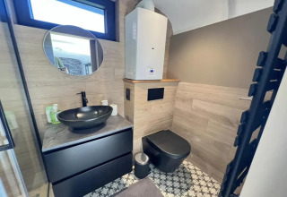 Baño moderno en Pine Tree Tiny Cottage, Bélgica, con lavabo y váter negros, decoración elegante y azulejos geométricos.