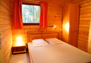 Træbeklædt soveværelse i De Boshut chalet i Belgien med dobbeltseng, lampe og udsigt til skov.
