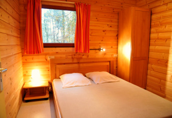 Holzverkleidetes Schlafzimmer im Chalet De Boshut in Belgien mit Doppelbett, Nachttisch und Fensterblick.
