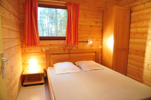 Chambre chaleureuse en bois du chalet De Boshut en Belgique, lit double, armoire et vue sur la forêt.
