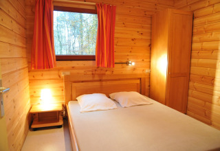 Chambre chaleureuse en bois du chalet De Boshut en Belgique, lit double, armoire et vue sur la forêt.