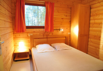 Cozy wood-paneled bedroom in De Boshut chalet, Belgium, with double bed, lamp, wardrobe, and forest view.