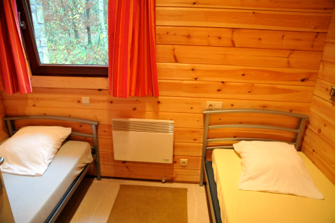 Et hyggeligt soveværelse med to enkeltsenge, trævægge og et vindue i chalet De Boshut i Belgien.