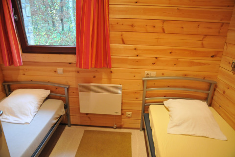 Chambre chaleureuse avec deux lits simples, murs en bois et fenêtre au chalet De Boshut en Belgique.