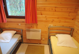 Chambre chaleureuse avec deux lits simples, murs en bois et fenêtre au chalet De Boshut en Belgique.
