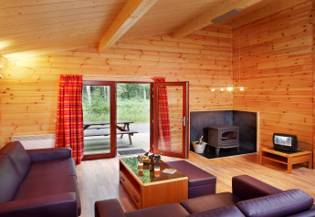 Wohnzimmer im Chalet De Boshut mit Holzverkleidung, Kamin, lila Sofas und Ausblick in die Natur.