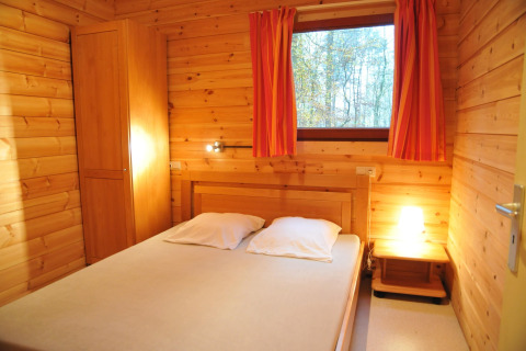 Chambre du chalet « De Boshut » en Belgique avec murs en bois, lit double et rideaux orange.