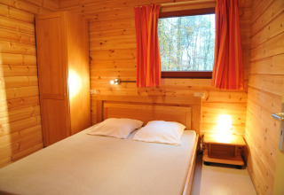 Chambre du chalet « De Boshut » en Belgique avec murs en bois, lit double et rideaux orange.