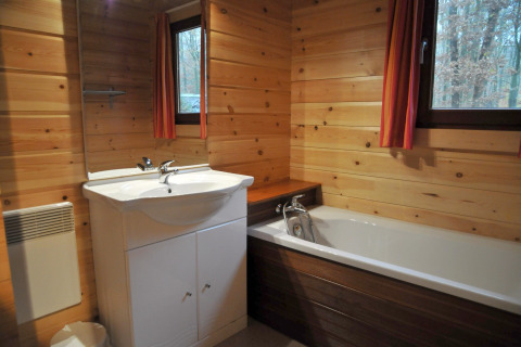 Badeværelse i chalet De Boshut i Belgien med trævægge, badekar og vinduer mod skovudsigt.