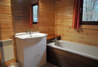 Badeværelse i chalet De Boshut i Belgien med trævægge, badekar og vinduer mod skovudsigt.