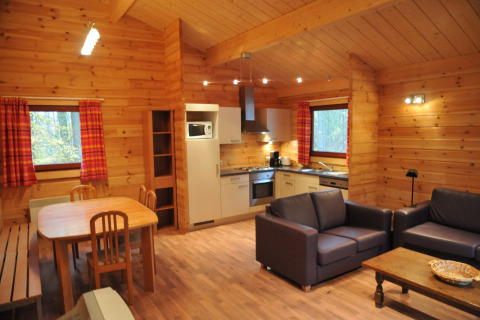 Vue intérieure du chalet « De Boshut » en Belgique avec cuisine, table à manger et salon confortable.