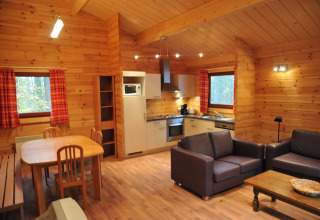 Vue intérieure du chalet « De Boshut » en Belgique avec cuisine, table à manger et salon confortable.