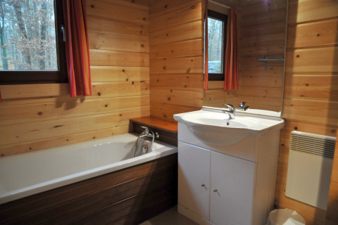Træbeklædt badeværelse med badekar, håndvask og vinduer på chalet ‘De Boshut’ i Belgien.