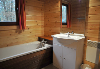 Træbeklædt badeværelse med badekar, håndvask og vinduer på chalet ‘De Boshut’ i Belgien.