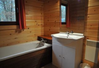 Salle de bain en bois avec baignoire, lavabo et fenêtres dans le chalet « De Boshut » en Belgique.