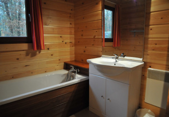 Wood-paneled bathroom with bathtub, sink, and windows in chalet ‘De Boshut’ located in Belgium.