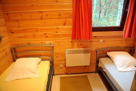 Værelse i chalet De Boshut i Belgien med to enkeltsenge, trævægge og vindue med udsigt til skov.